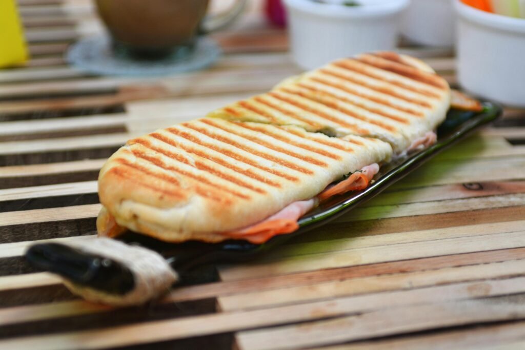 Tasty grilled panini sandwich with ham and cheese on a wooden table.